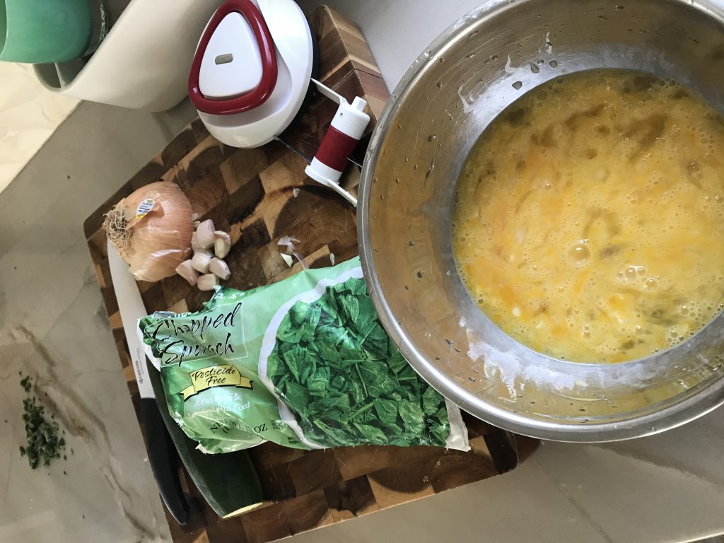 Whole30 Spinach Onion Zucchini Frittata ingredients including eggs, onion, zucchini and spinach on a cutting board